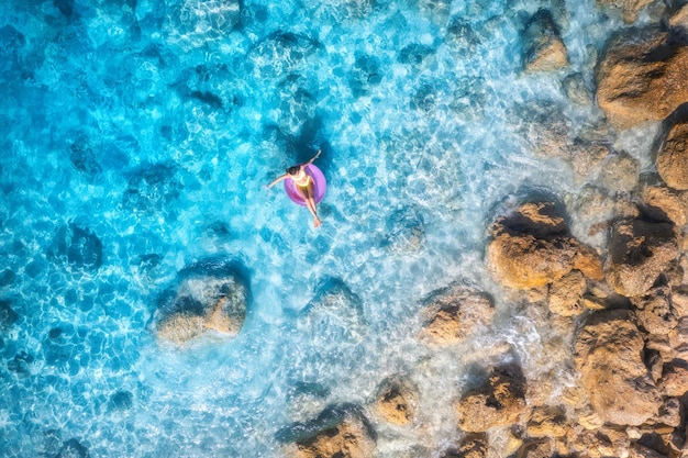 Vista aerea di una giovane donna che nuota con l'anello di nuoto nel mare blu