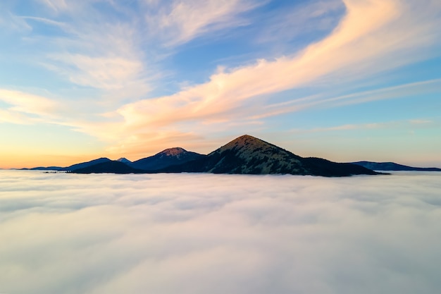 Vista aerea di una grande montagna sopra nuvole dense bianche all'alba luminosa.