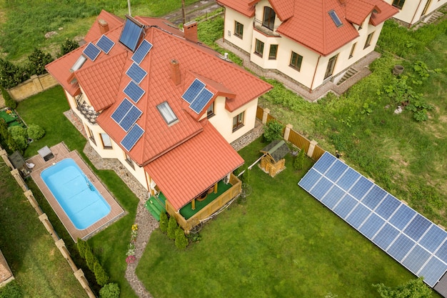Vista aerea di una nuova casa autonoma con pannelli solari e termosifoni sul tetto e cortile verde con piscina blu.