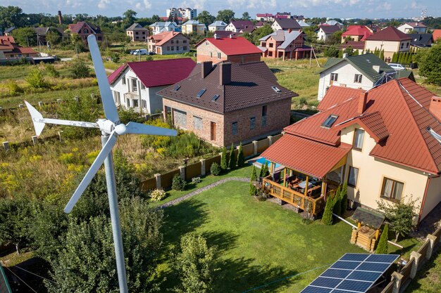 Vista aerea di una nuova casa autonoma con pannelli solari, radiatori di riscaldamento dell'acqua sul tetto e turbina eolica sul cortile verde.