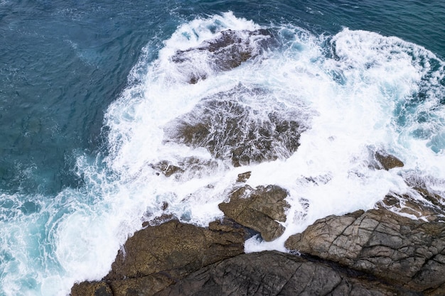 Vista aerea Drone fotocamera dall'alto verso il basso delle rocce della spiaggia in un oceano blu Superficie del mare turchese Incredibili onde del mare che si infrangono sul paesaggio marino delle rocce Immagine di alta qualità delle onde del mare a Phuket Thailandia