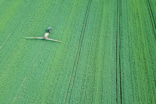 Vista aerea Macchine agricole che spruzzano sostanze chimiche sul grande campo verde, sfondo primaverile agricolo.