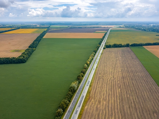 Vista aerea panoramica di un'autostrada con auto su di esso, campi, piantagione di alberi al tramonto estivo. Vista dall'alto dal drone volante.