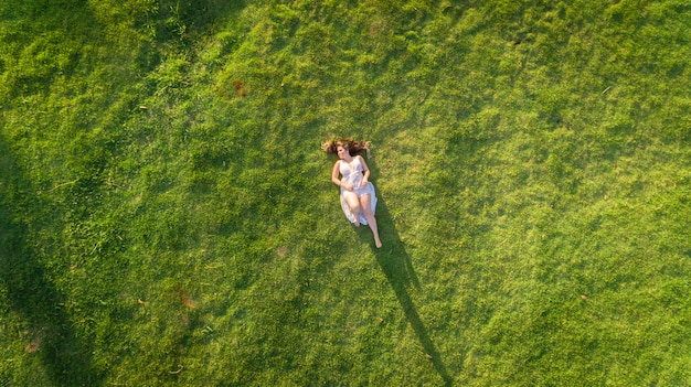 Vista aerea. Ragazza che si trova e che riposa sul prato inglese il giorno soleggiato nel parco su erba.