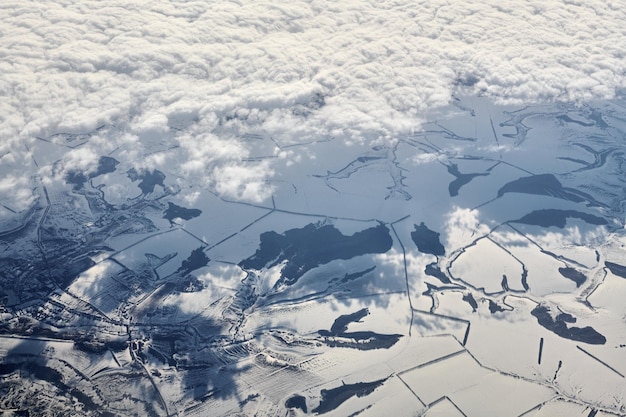 Vista aerea sopra le nuvole dall'alto ai fiumi innevati, campi e strade invernali aria fresca e gelida