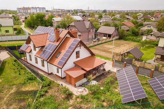Vista aerea superiore del nuovo moderno cottage casa residenziale con sistema fotovoltaico solare lucido blu pannelli fotovoltaici sul tetto. Concetto di produzione di energia verde ecologica rinnovabile.