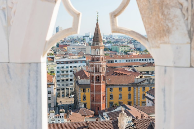 Vista alla torre di San Gottardo dal tetto del Duomo attraverso una recinzione di marmo decorata. Milano, Italia