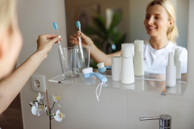 Vista allo specchio sulla bella femmina bionda che prende lo spazzolino da denti per lavarsi i denti al mattino