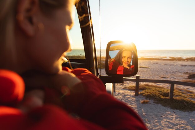 Vista anteriore da vicino di una donna caucasica all'interno di un'auto a tetto aperto, sorridente e guardando il suo riflesso in uno specchio laterale