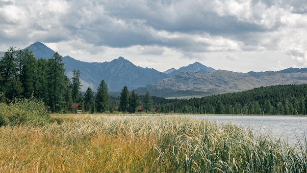 Vista atmosferica di un lago di montagna con campeggio sulla riva in una foresta di conifere sullo sfondo delle montagne e di un drammatico cielo nuvoloso