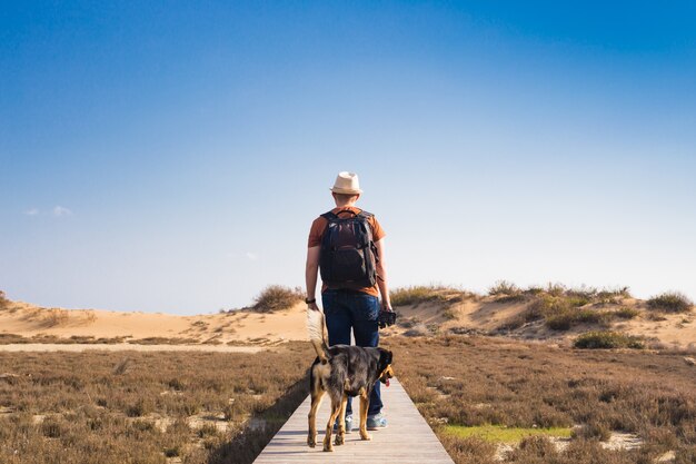 Vista da dietro di un uomo che cammina con il suo cane su una strada che conduce attraverso un bellissimo paesaggio.