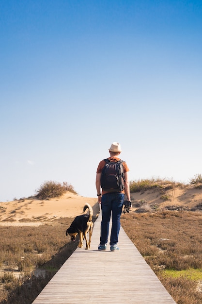 Vista da dietro di un uomo che cammina con il suo cane su una strada che conduce attraverso un bellissimo paesaggio.