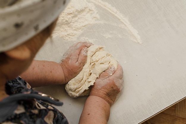 Vista da dietro la spalla di una donna anziana che impasta la pasta con le mani alla vecchia maniera