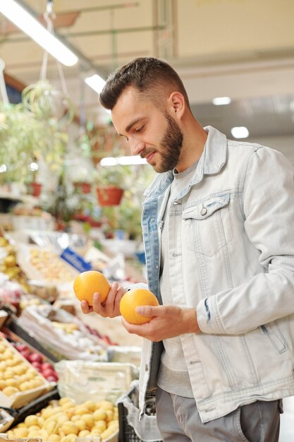 Vista da sopra la spalla dell'uomo barbuto in piedi al bancone alimentare e l'acquisto di agrumi per rafforzare l'immunità al mercato