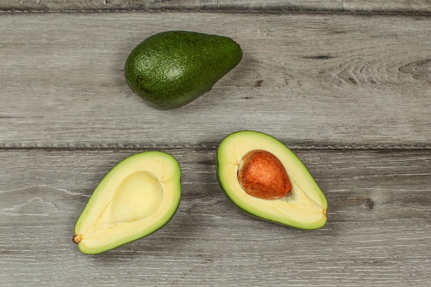 Vista da tavolo, avocado tagliato a metà, pera intera sopra, posta su una scrivania in legno grigio.