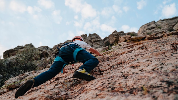 Vista dal basso di un bambino con i capelli castani che scala una montagna