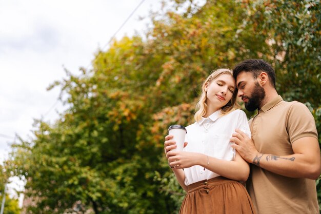 Vista dal basso di una giovane coppia felice innamorata in piedi abbracciata con gli occhi chiusi al parco cittadino Bell'uomo tatuato e bella donna che cammina trascorrendo del tempo