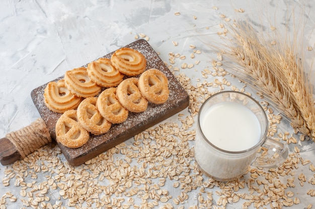 vista dal basso vari biscotti sul tagliere spighe di grano bicchiere di latte avena sparsa sul tavolo