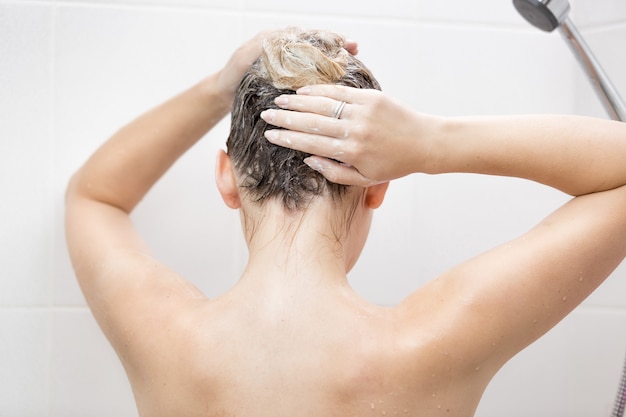 Vista dal retro di una donna sexy che lava i capelli con lo shampoo