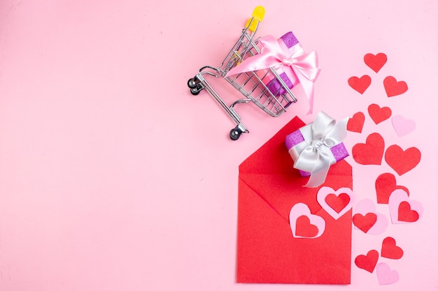 vista dall'alto adesivi cuore rosso busta rossa regalo in piccolo carrello del mercato su sfondo rosa posto libero