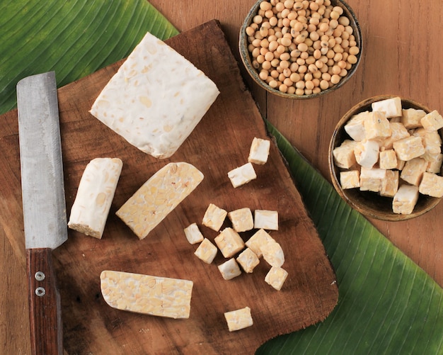 Vista dall'alto Affettare il tempeh crudo sul tagliere di legno sopra il tavolo marrone rustico