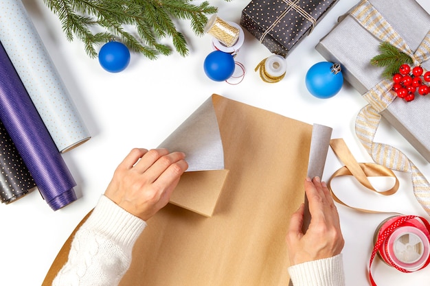 Vista dall'alto alle mani di donna che imballano scatole regalo di Natale sul tavolo bianco