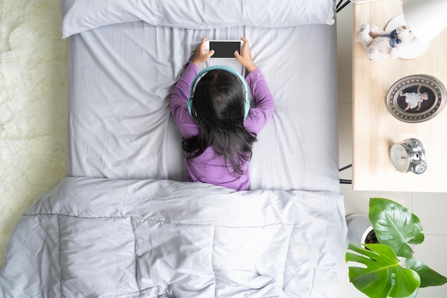 Vista dall'alto Bambina asiatica che gioca con lo smartphone sdraiato sul letto