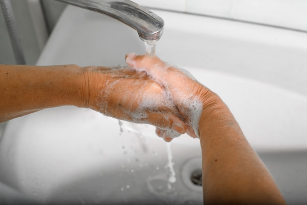 Vista dall'alto closeup donna anziana lava le mani rugose con sapone disinfetta da batteri e virus