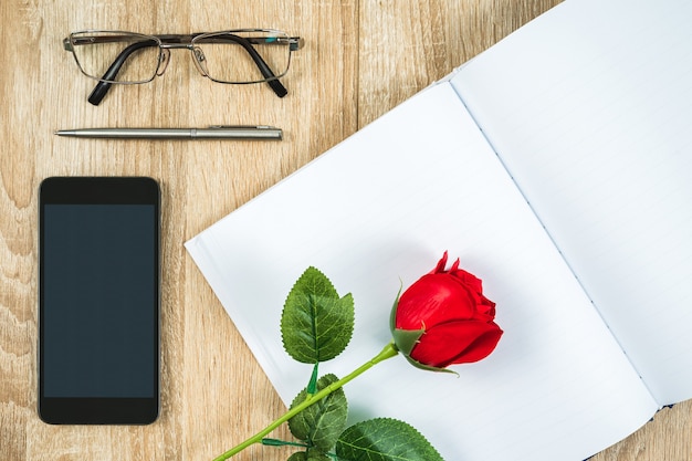 Vista dall'alto colpo di rose rosse diario vuoto vuoto notebook e occhiali con lo smartphone sulla tavola di legno, concetto di San Valentino