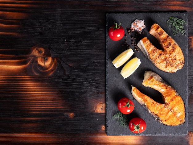 Vista dall'alto con anelli di salmone disposti su un piatto di pietra. Pomodori e limone