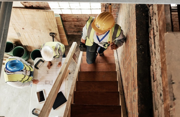 Vista dall'alto costruzione e fasi con l'ingegnere costruttore e il team che parlano per il progetto di collaborazione di progettazione del progetto o il brainstorming Architettura hardhat e architetto con lavoro di squadra e discussione