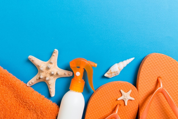 Vista dall'alto degli accessori piatti da spiaggia. bottiglia di crema solare con conchiglie, stelle marine, asciugamano e infradito su sfondo colorato con spazio di copia.