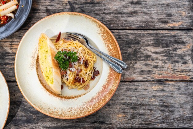 Vista dall'alto degli spaghetti alla carbonara con prosciutto croccante e salsa di panna bianca in piatto di ceramica su tavola di legno