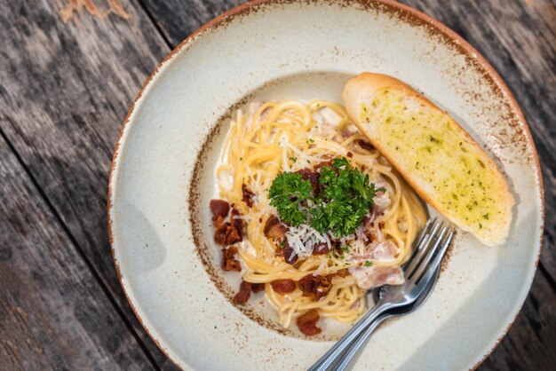 Vista dall'alto degli spaghetti alla carbonara con prosciutto croccante e salsa di panna bianca in piatto di ceramica su tavola di legno