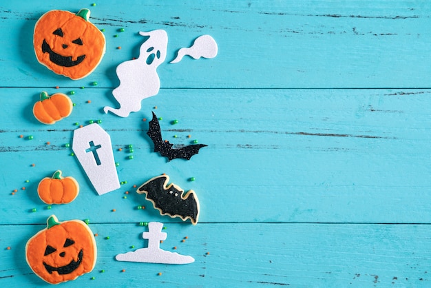 Vista dall'alto dei biscotti di zucchero di pan di zenzero con glassa al forno decorata in festa di Halloween su sfondo blu con spazio di copia e disposizione piatta.