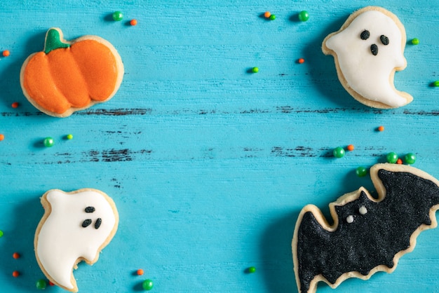 Vista dall'alto dei biscotti di zucchero di pan di zenzero con glassa al forno decorata in festa di Halloween su sfondo blu con spazio di copia e disposizione piatta.