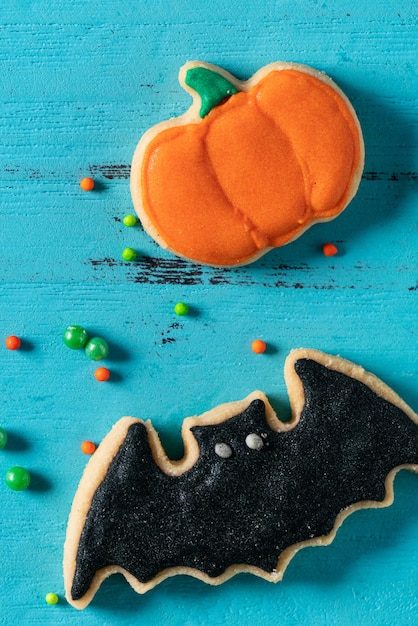 Vista dall'alto dei biscotti di zucchero di pan di zenzero con glassa al forno decorata in festa di Halloween su sfondo blu con spazio di copia e disposizione piatta.