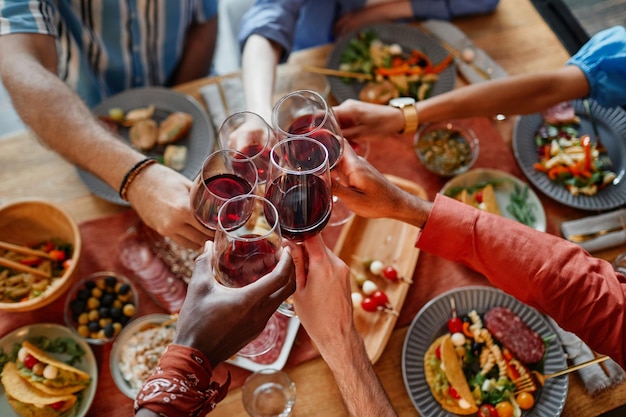 Vista dall'alto dei giovani che brindano con bicchieri di vino mentre festeggiano insieme a cena