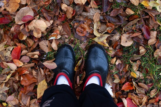 Vista dall'alto dei piedi con scarpe di gomma sullo sfondo del fogliame autunnale marrone caduto appassito