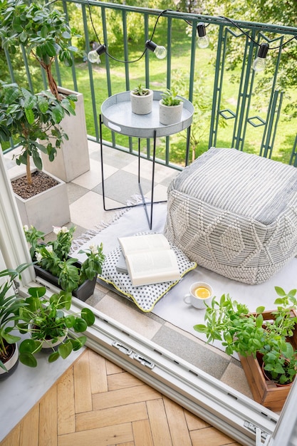 Vista dall'alto del balcone con luci tazza di piante fresche con libro aperto da tè e pouf materiale nella foto reale