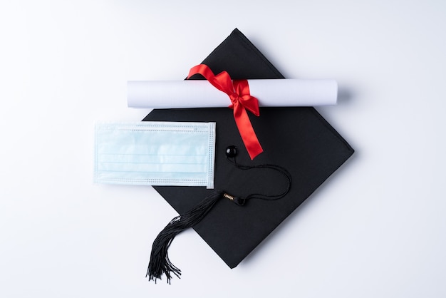 Vista dall'alto del berretto accademico quadrato di laurea con diploma di laurea e maschera isolata su sfondo bianco della tavola.