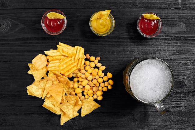 Vista dall'alto del bicchiere di birra e spuntini con salsa sul tavolo di legno nero