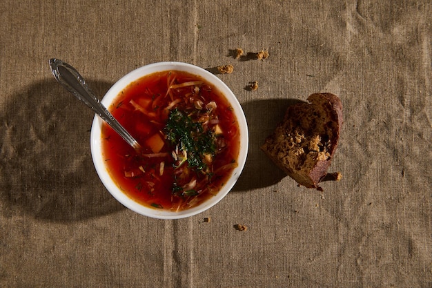 Vista dall'alto del borscht, zuppa tradizionale ucraina con verdure sane e pomodori, pane integrale e briciole su una tovaglia di lino