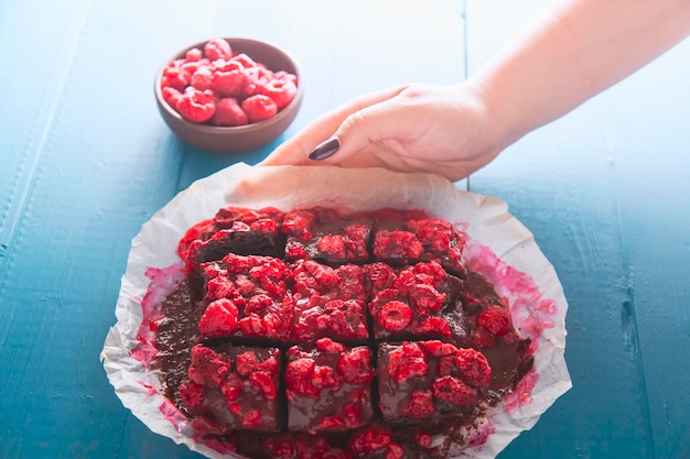 Vista dall'alto del brownie al lampone fatto in casa senza glutine su un tavolo di legno vintage blu la mano di una donna elegante anonima sta servendo la torta