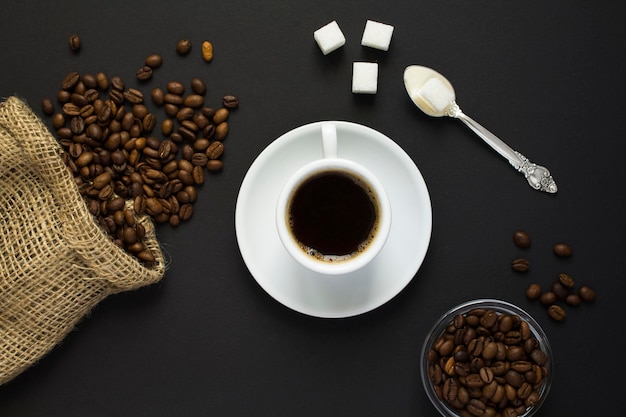 Vista dall'alto del caffè nero nella tazza bianca e dei chicchi di caffè sullo sfondo nero Primo piano