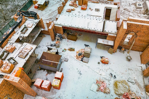 Vista dall'alto del cantiere Costruzione di una casa di mattoni rossi Costruire in inverno Colpo dettagliato del cantiere Neve in cantiere