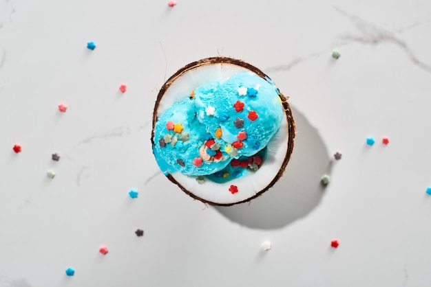 Vista dall'alto del delizioso gelato blu con spruzzi su metà cocco su sfondo grigio marmo