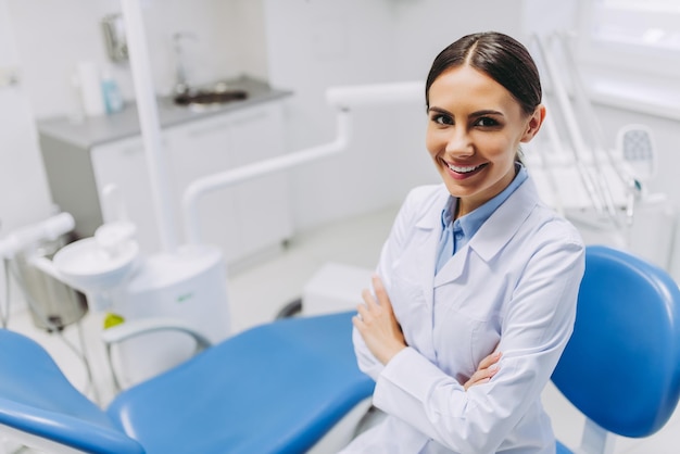 Vista dall'alto del dentista sorridente con le mani incrociate che guardano la telecamera nella clinica dentale