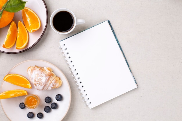 Vista dall'alto del diario vuoto e della tazza di caffè, croissant, mirtilli e arance succose