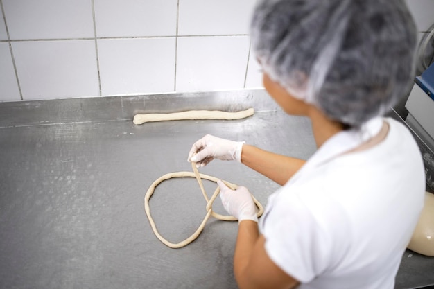 Vista dall'alto del fornaio in uniforme bianca e retina per capelli che impasta e prepara la pasta per la cottura